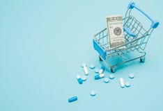 Dolary, pigułki i wózek na zakupy na błękitnym tle, Apteki pojęcie kosmos kopii zdjęcia stock Dolary, pigułki i wózek na zakupy na błękitnym tle, Apteki pojęcie kosmos kopii zdjęcia stock