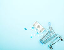 Dolary, pigułki i wózek na zakupy na błękitnym tle, Apteki pojęcie kosmos kopii obrazy royalty free Dolary, pigułki i wózek na zakupy na błękitnym tle, Apteki pojęcie kosmos kopii obrazy royalty free
