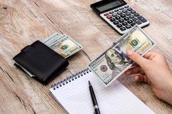 Dollar i hand, räknemaskin, notepad och penna på en träbakgrund royaltyfri fotografi Dollar i hand, räknemaskin, notepad och penna på en träbakgrund royaltyfri fotografi