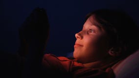 Dolly geschoten Kaukasisch meisje in bed het spelen tablet in Internet in donkerblauw licht onder blacket Dolly geschoten Kaukasisch meisje in bed het spelen tablet in Internet in donkerblauw licht onder blacket