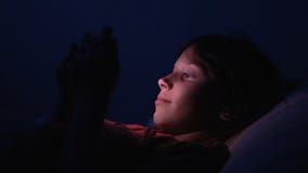 Dolly geschoten Kaukasisch meisje in bed het spelen tablet in Internet in donkerblauw licht onder blacket Dolly geschoten Kaukasisch meisje in bed het spelen tablet in Internet in donkerblauw licht onder blacket
