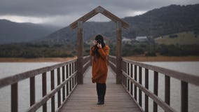 Donkerbruine vrouwenfotograaf met oranje trenchcoat op een brug royalty-vrije stock foto's Donkerbruine vrouwenfotograaf met oranje trenchcoat op een brug royalty-vrije stock foto's