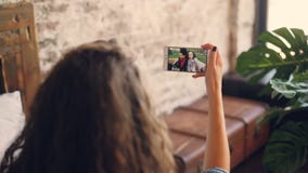 Donkerharige het spreken aan vrouwelijke vrienden online met smartphone, meisje bekijkt het scherm, houdend apparaat en stock videobeelden Donkerharige het spreken aan vrouwelijke vrienden online met smartphone, meisje bekijkt het scherm, houdend apparaat en stock videobeelden