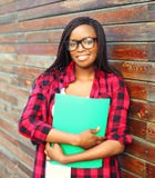 Donna africana sorridente del ritratto giovane in vetri che tengono cartella sopra fondo Immagine Stock Donna africana sorridente del ritratto giovane in vetri che tengono cartella sopra fondo Immagine Stock