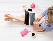Donna alla moda che si siede sul pavimento e che per mezzo del computer portatile fotografia stock Donna alla moda che si siede sul pavimento e che per mezzo del computer portatile fotografia stock