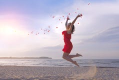 Donna bella di salto in vestito rosso che getta i petali rosa sulla spiaggia fotografia stock libera da diritti Donna bella di salto in vestito rosso che getta i petali rosa sulla spiaggia fotografia stock libera da diritti