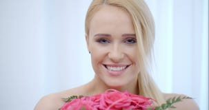 Donna bionda sorridente che odora le rose rosa video d archivio Donna bionda sorridente che odora le rose rosa video d archivio