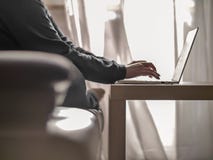 Donna che scrive su un computer portatile mentre sedendosi su un sofà contro lo sfondo di una finestra fotografie stock libere da diritti Donna che scrive su un computer portatile mentre sedendosi su un sofà contro lo sfondo di una finestra fotografie stock libere da diritti