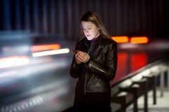 Donna con il telefono cellulare che cammina alla notte accanto alla strada principale fotografia stock libera da diritti Donna con il telefono cellulare che cammina alla notte accanto alla strada principale fotografia stock libera da diritti