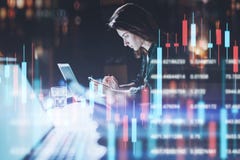 Donna di affari che si siede all'ufficio di notte in computer portatile anteriore con i grafici finanziari e che per mezzo del su immagini stock Donna di affari che si siede all'ufficio di notte in computer portatile anteriore con i grafici finanziari e che per mezzo del su immagini stock
