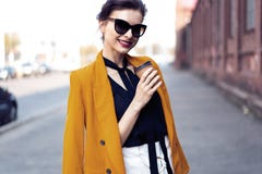 Donna di modo del ritratto in occhiali da sole che cammina sulla via Porta il rivestimento giallo, sorridente per parteggiare fotografia stock libera da diritti Donna di modo del ritratto in occhiali da sole che cammina sulla via Porta il rivestimento giallo, sorridente per parteggiare fotografia stock libera da diritti