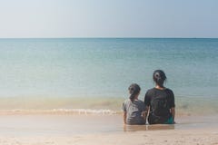 Donna e bambini che si siedono di nuovo alla parte posteriore sulla spiaggia di sabbia e che guardano alla vista sul mare immagine stock libera da diritti Donna e bambini che si siedono di nuovo alla parte posteriore sulla spiaggia di sabbia e che guardano alla vista sul mare immagine stock libera da diritti