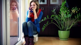 Donna graziosa che sorride alla macchina fotografica che si siede sul radiatore e sul tè caldo bevente stock footage Donna graziosa che sorride alla macchina fotografica che si siede sul radiatore e sul tè caldo bevente stock footage