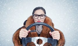 Donna importante in vetri e una pelliccia che conduce un'automobile nella neve Su priorità bassa blu immagine stock Donna importante in vetri e una pelliccia che conduce un'automobile nella neve Su priorità bassa blu immagine stock