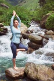 Donna nella posa dell'albero di Vrikshasana di asana di yoga alla cascata all'aperto fotografia stock Donna nella posa dell'albero di Vrikshasana di asana di yoga alla cascata all'aperto fotografia stock