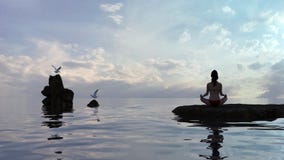 Donna nella posizione di loto di yoga da acqua al crepuscolo con i gabbiani vicini immagine stock Donna nella posizione di loto di yoga da acqua al crepuscolo con i gabbiani vicini immagine stock