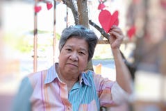 Donna più anziana che tiene la carta rossa del cuore & che sorride alla macchina fotografica E felice Fotografia Stock Donna più anziana che tiene la carta rossa del cuore & che sorride alla macchina fotografica E felice Fotografia Stock