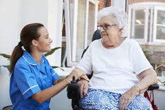 Donna senior che si siede in sedia a rotelle motorizzata che parla con l'infermiere In Retirement Home immagini stock libere da diritti Donna senior che si siede in sedia a rotelle motorizzata che parla con l'infermiere In Retirement Home immagini stock libere da diritti