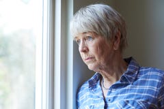 Donna senior che soffre dalla depressione che guarda dalla finestra Immagini Stock Libere da Diritti Donna senior che soffre dalla depressione che guarda dalla finestra Immagini Stock Libere da Diritti