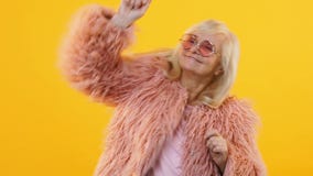 Donna senior felice che balla sul movimento lento giallo del fondo, giovane partito ritenente stock footage Donna senior felice che balla sul movimento lento giallo del fondo, giovane partito ritenente stock footage