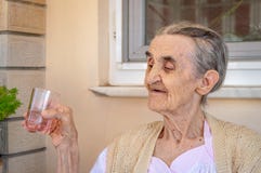 Donna senior molto anziana nel balcone che tiene un bicchiere d'acqua in sua mano fotografia stock libera da diritti Donna senior molto anziana nel balcone che tiene un bicchiere d'acqua in sua mano fotografia stock libera da diritti