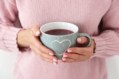 Donna in un maglione tricottato rosa che tiene una grande tazza con un cuore fotografia stock Donna in un maglione tricottato rosa che tiene una grande tazza con un cuore fotografia stock