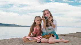 Dos adolescentes se están sentando en una playa arenosa, en Internet en teléfono foto de archivo libre de regalías Dos adolescentes se están sentando en una playa arenosa, en Internet en teléfono foto de archivo libre de regalías