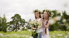 Dos amigas en guirnalda con la situación del ramo de las flores en campo floreciente Muchachas del adolescente que presentan en c almacen de video Dos amigas en guirnalda con la situación del ramo de las flores en campo floreciente Muchachas del adolescente que presentan en c almacen de video