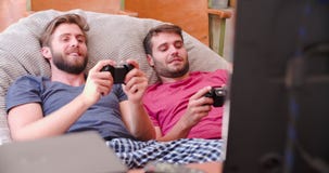 Dos amigos masculinos en los pijamas que juegan al videojuego junto almacen de video Dos amigos masculinos en los pijamas que juegan al videojuego junto almacen de video