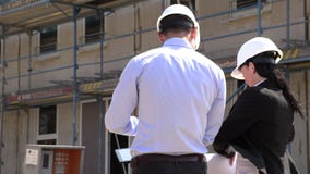 Dos arquitectos en los cascos blancos discuten un plan en un emplazamiento de la obra Dos arquitectos en los cascos blancos discuten un plan en un emplazamiento de la obra