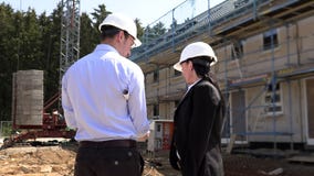 Dos arquitectos un hombre y una mujer en la construcci?n en los cascos blancos Dos arquitectos un hombre y una mujer en la construcci?n en los cascos blancos