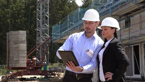 Dos arquitectos un hombre y una mujer en la construcci?n en los cascos blancos Dos arquitectos un hombre y una mujer en la construcci?n en los cascos blancos