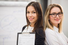 Dos compañeros de trabajo de las empresarias que se colocan en una oficina y que sonríen positivamente en la cámara mientras que fotos de archivo Dos compañeros de trabajo de las empresarias que se colocan en una oficina y que sonríen positivamente en la cámara mientras que fotos de archivo