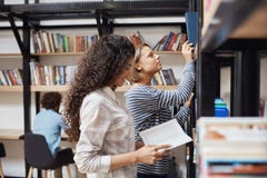 Dos estudiantes alegres jovenes en la ropa casual que coloca los estantes cercanos en la biblioteca de universidad que mira a tra Fotos de archivo libres de regalías Dos estudiantes alegres jovenes en la ropa casual que coloca los estantes cercanos en la biblioteca de universidad que mira a tra Fotos de archivo libres de regalías