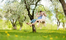 Dos hermanas lindas que se divierten en un oscilación en jardín viejo floreciente del manzano al aire libre en día de primavera s fotos de archivo libres de regalías Dos hermanas lindas que se divierten en un oscilación en jardín viejo floreciente del manzano al aire libre en día de primavera s fotos de archivo libres de regalías