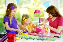Dos hermanas lindas y su madre joven que envuelven los regalos en papel de embalaje colorido Fotos de archivo Dos hermanas lindas y su madre joven que envuelven los regalos en papel de embalaje colorido Fotos de archivo