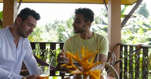 Dos hombres que usan la tableta que se sienta en la terraza que habla, web que practica surf casual joven del verano de la pantal almacen de video Dos hombres que usan la tableta que se sienta en la terraza que habla, web que practica surf casual joven del verano de la pantal almacen de video