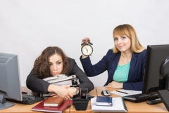 Dos muchachas en la oficina al final del día, una con una sonrisa, celebrando un reloj, otras mentiras cansadas en carpetas Imagen de archivo Dos muchachas en la oficina al final del día, una con una sonrisa, celebrando un reloj, otras mentiras cansadas en carpetas Imagen de archivo