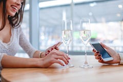 Dos muchachas se están sentando en un café, usando los teléfonos móviles y el champán de consumición fotografía de archivo Dos muchachas se están sentando en un café, usando los teléfonos móviles y el champán de consumición fotografía de archivo