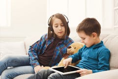 Dos niños con los artilugios en el sofá en casa Foto de archivo Dos niños con los artilugios en el sofá en casa Foto de archivo