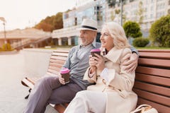 Dos pensionistas se están sentando en un banco con un vidrio de café en sus manos Sientan el abarcamiento y la sonrisa Foto de archivo Dos pensionistas se están sentando en un banco con un vidrio de café en sus manos Sientan el abarcamiento y la sonrisa Foto de archivo