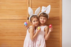 Dos pequeñas hermanas encantadoras divertidas en los vestidos con los oídos de conejo blancos en sus cabezas sostienen los huevos imagen de archivo libre de regalías Dos pequeñas hermanas encantadoras divertidas en los vestidos con los oídos de conejo blancos en sus cabezas sostienen los huevos imagen de archivo libre de regalías