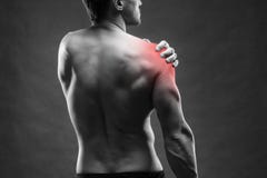 Douleur dans l'épaule Fuselage mâle musculaire Bodybuilder beau posant sur le fond gris images libres de droits Douleur dans l'épaule Fuselage mâle musculaire Bodybuilder beau posant sur le fond gris images libres de droits
