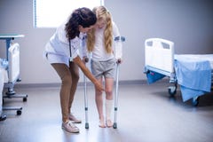 Doutor fêmea que ajuda à menina a andar com as muletas na divisão imagem de stock Doutor fêmea que ajuda à menina a andar com as muletas na divisão imagem de stock