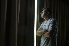 Dramatic Light Portrait Of Young Sad And Depressed Attractive Man At Home Looking Through Room Window Thoughtful And Pensive Lost Stock Images