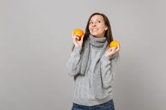 Dreamful young woman in gray sweater scarf looking up holding oranges isolated on grey background in studio. Healthy royalty free stock photo Dreamful young woman in gray sweater scarf looking up holding oranges isolated on grey background in studio. Healthy royalty free stock photo