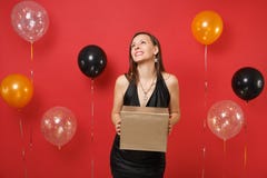 Dreamy happy girl in black dress celebrating looking up hold golden box with gift present on bright red background air