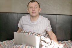 Dreamy young man sitting in bed with a laptop under the covers royalty free stock photo Dreamy young man sitting in bed with a laptop under the covers royalty free stock photo