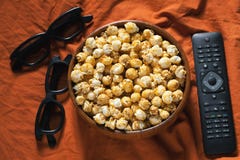 Drewniany puchar z słodkim popkornem, TV pilot do tv i 3D szkłami na pomarańczowej pościeli, Odgórny widok Przekąski i jedzenie d fotografia stock Drewniany puchar z słodkim popkornem, TV pilot do tv i 3D szkłami na pomarańczowej pościeli, Odgórny widok Przekąski i jedzenie d fotografia stock
