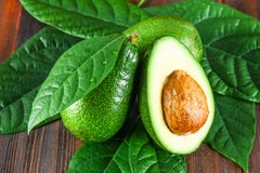 Drie groene ruwe rijpe avocadovruchten en een besnoeiing half met een been met bladeren op een bruine houten lijst Stock Afbeeldingen Drie groene ruwe rijpe avocadovruchten en een besnoeiing half met een been met bladeren op een bruine houten lijst Stock Afbeeldingen